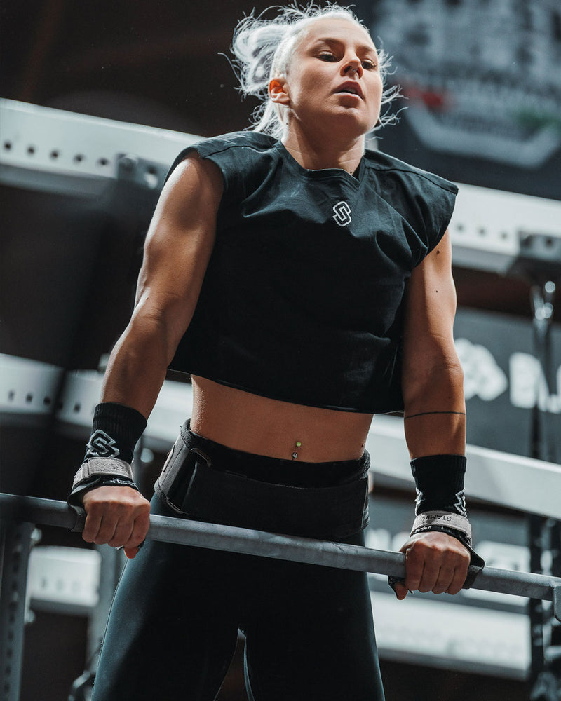 Atleta donna esegue muscle-up alla sbarra indossando paracalli Hybrid STMN Fitness e polsiere nere